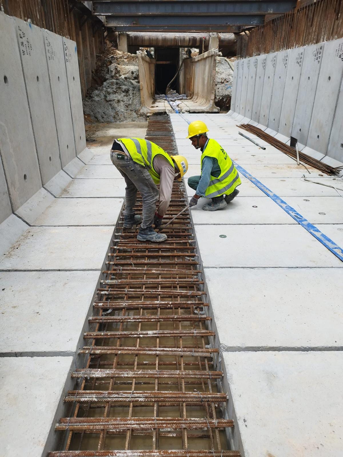 Buildwick site workers in full PPE — hard hats, safety vests and gloves — installing rebar for an RC drain